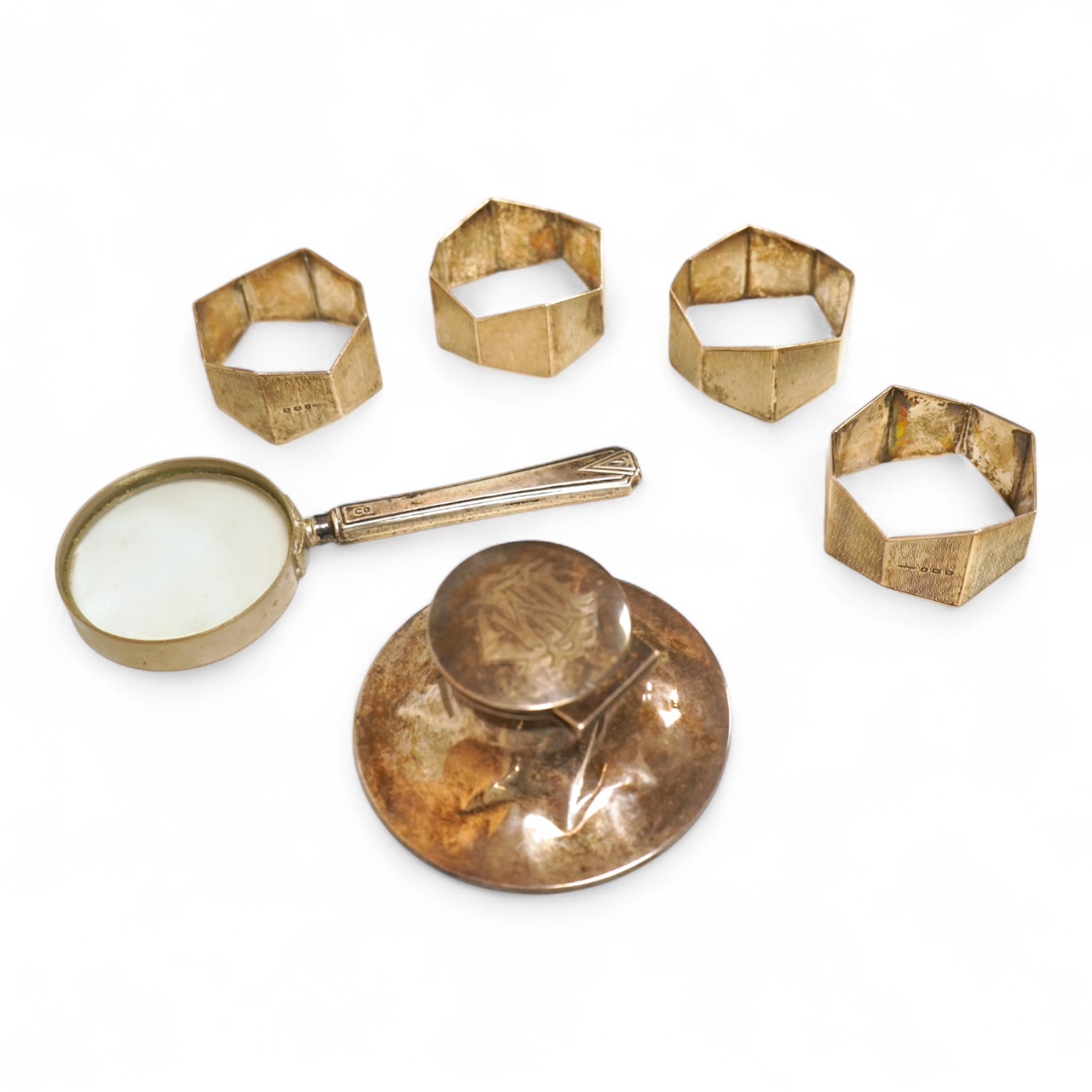 A small silver mounted capstan inkwell, a set of four George V engine turned silver napkin rings and a silver handled magnifying glass.